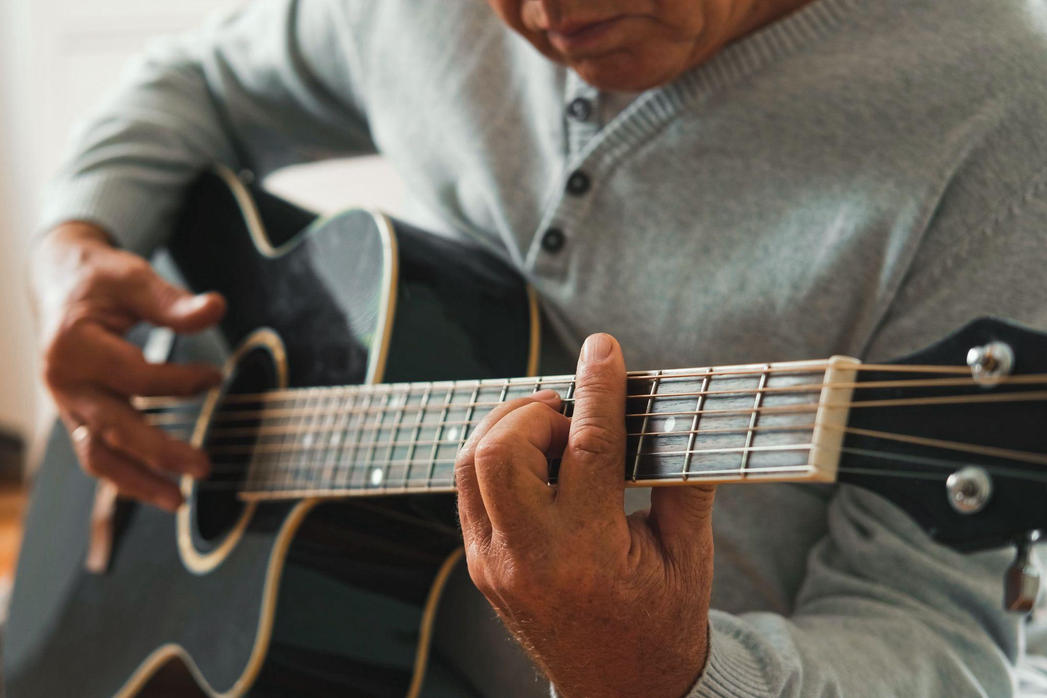 An older adult is sitting down and playing a guitar as an activity to support brain health.