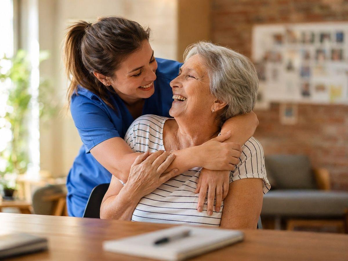 A caregiver giving a senior a hug, while both smiling at each other happily in an assisted living community.